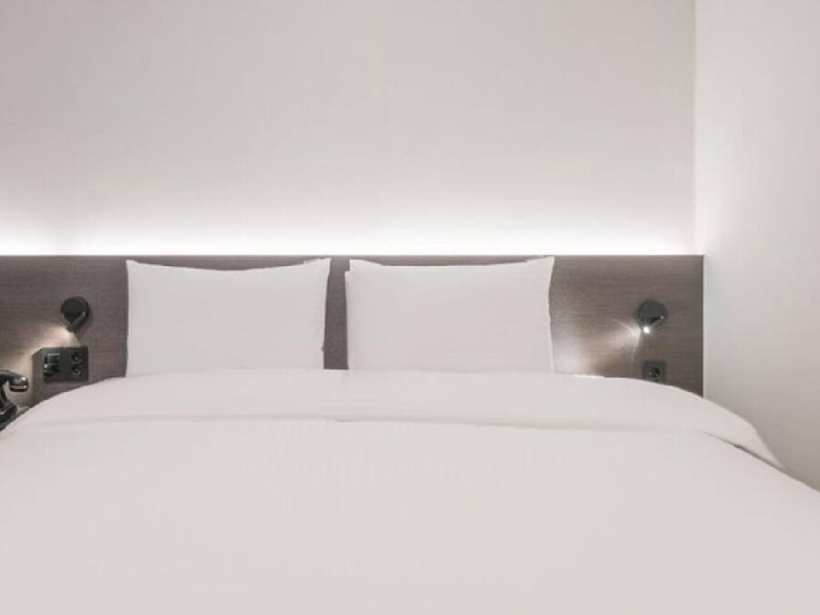 A modern hotel room with a large bed, a bedside telephone, and a wall-mounted light fixture.