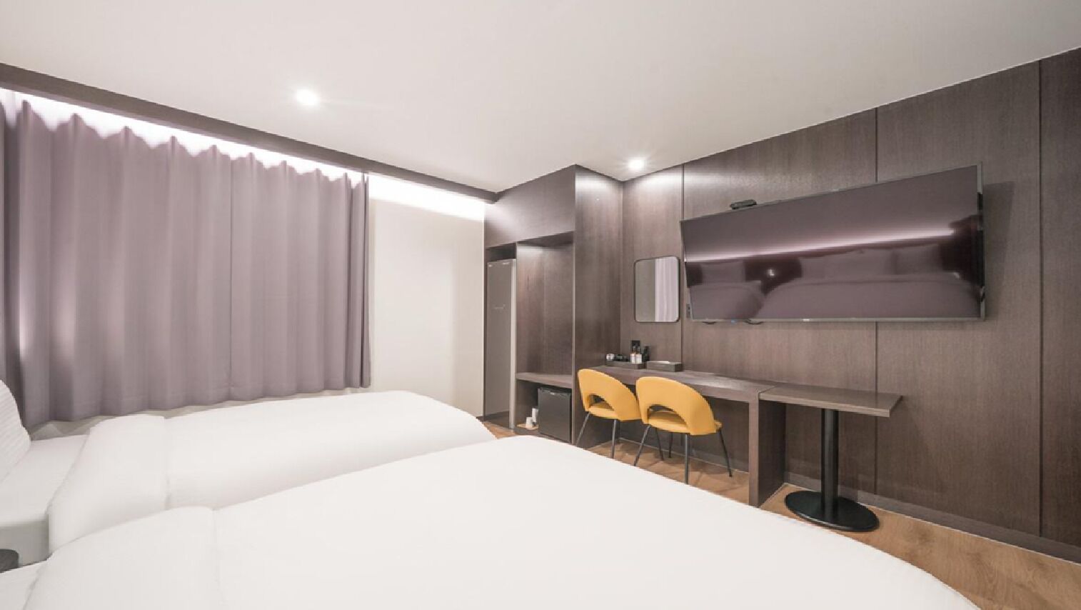 Habitación de hotel con dos camas, un escritorio con sillas, un televisor de pantalla plana y un espejo.