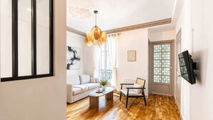 Een moderne woonkamer met een houten vloer, een witte bank, een salontafel, een hanglamp en een deur met ruitverdeling.