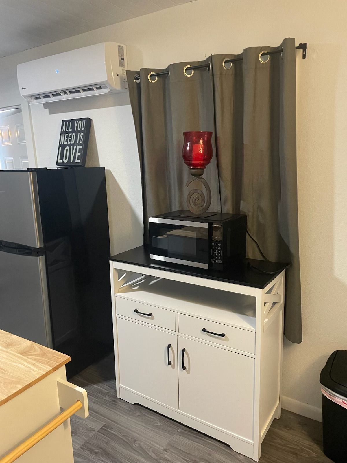 A kitchenette with a microwave on a white cabinet, a refrigerator, a trash bin, and a sign on the wall.