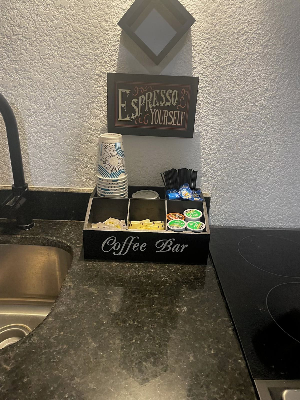 Uma bancada de cozinha com espaço para café, incluindo cafeteira, xícaras e cápsulas de café.
