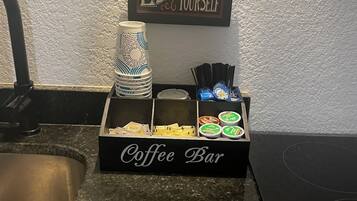 Uma bancada de cozinha com espaço para café, incluindo cafeteira, xícaras e cápsulas de café.