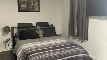 A bedroom with a bed, a bedside table, a lamp, a framed picture on the wall, and a window with curtains.