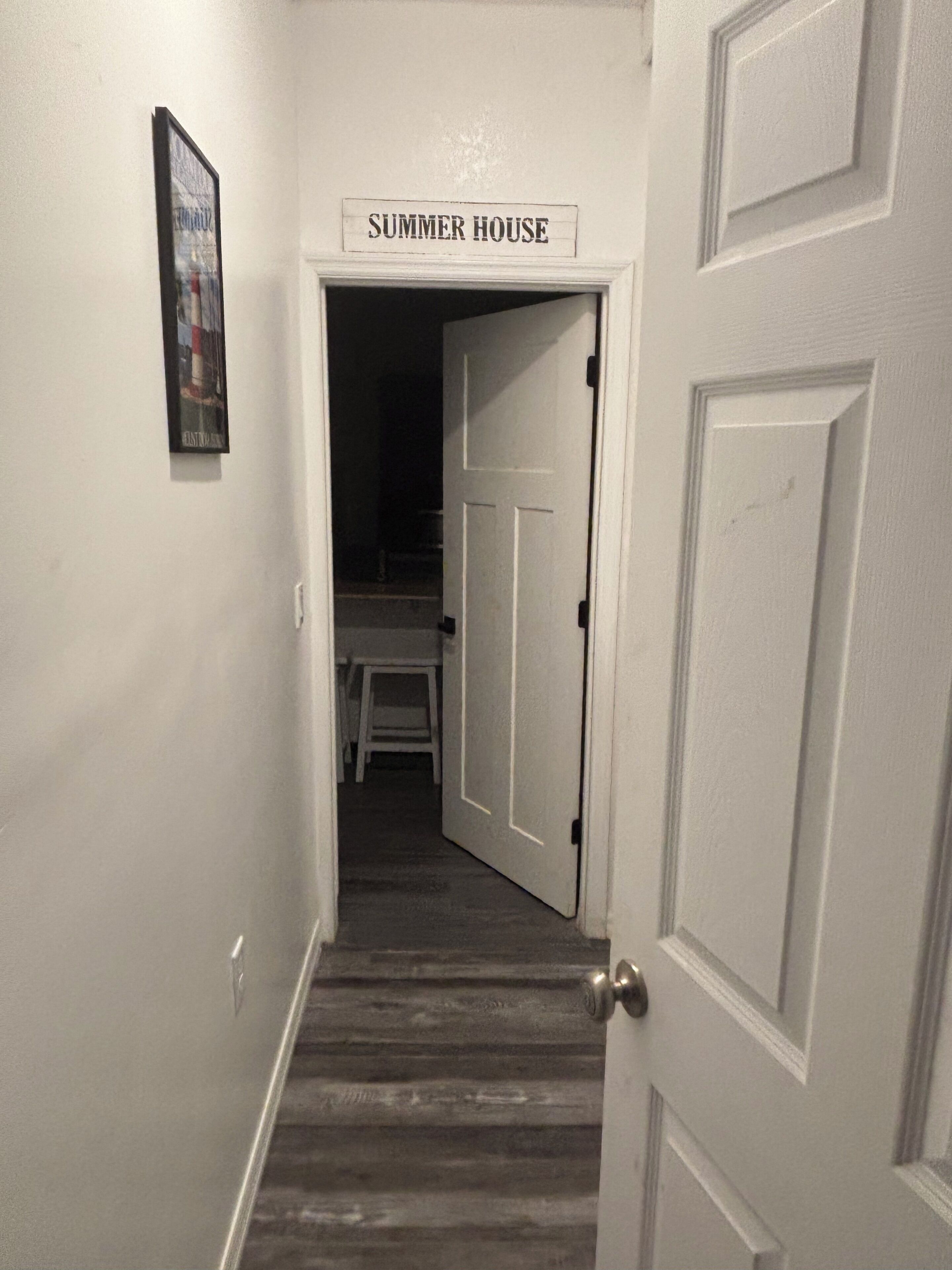 Un pasillo que conduce a una habitación con la leyenda 'SUMMER HOUSE', con piso de madera y paredes blancas.