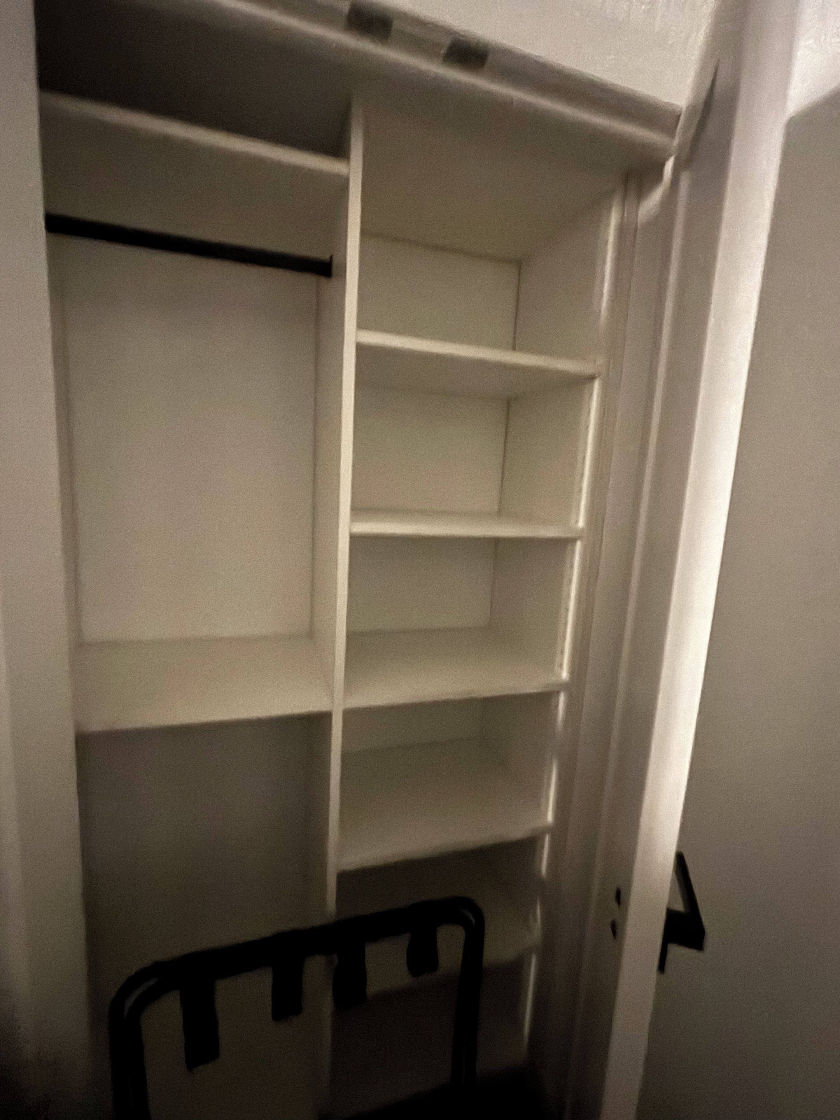 A closet with multiple shelves and a chair.