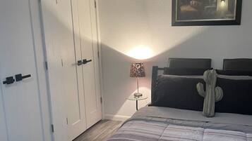 A bedroom with a bed, a cactus decoration, a framed picture on the wall, and a bedside lamp.
