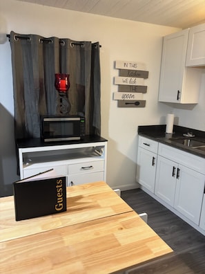 Une cuisine moderne avec des meubles blancs, un plan de travail noir, un four à micro-ondes, un porte-bougie rouge et un panneau décoratif au mur.