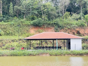 A building with a red-tiled roof, surrounded by lush greenery and a body of water. - Jungle Lake Resort - Sakleshpur (Sakleshpur)