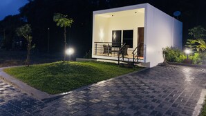 A modern, single-story building with a flat roof, a balcony with outdoor seating, and a paved entrance area.
