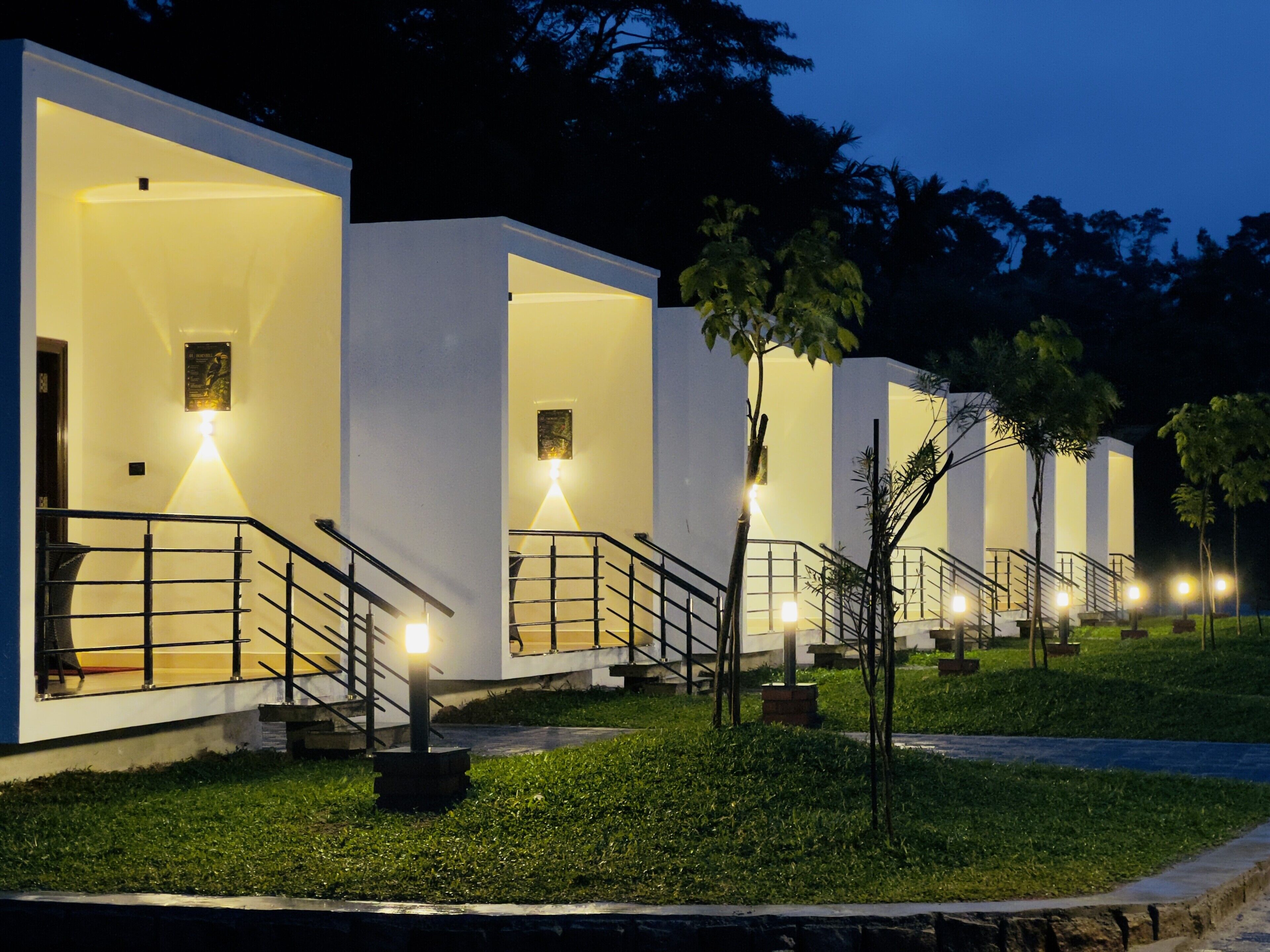 A row of modern, well-lit buildings with outdoor staircases and small trees in front.