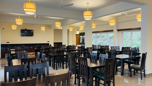 A spacious dining area with multiple tables and chairs, ceiling fans, and pendant lighting.