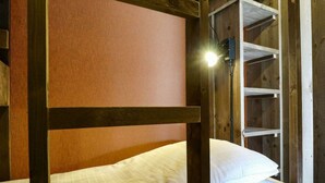 A bunk bed with a headboard, a shelf unit, and a wall-mounted light fixture.