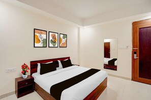 A hotel room with a bed, a nightstand, a vase with flowers, and three framed artworks on the wall.