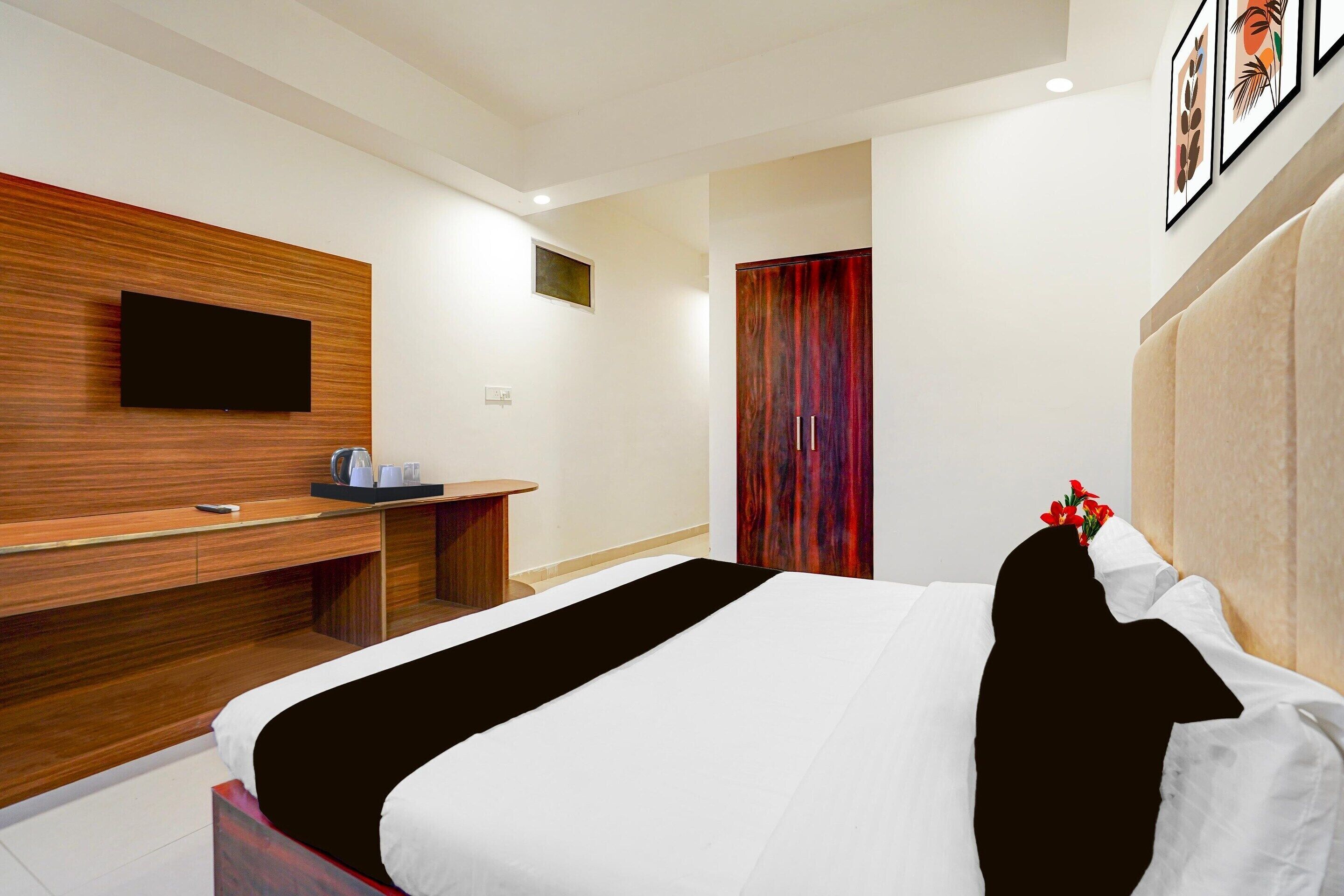 A modern hotel room with a large bed, a wooden desk, a flat-screen TV, and a red curtain.