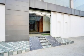 A modern building entrance with a glass door, a tiled floor, and a ramp leading to the door.