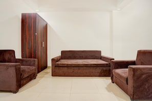 A room with a brown sofa, two armchairs, and a wooden wardrobe.