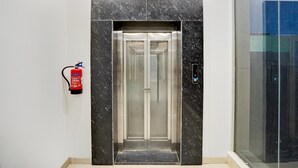 An elevator with a marble facade, a fire extinguisher mounted on the wall, and a glass door.