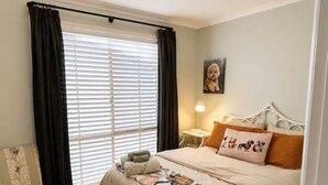 Un dormitorio con cama, una silla, una lámpara y un cuadro en la pared.