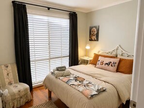 Een slaapkamer met een bed, een stoel, een lamp en een schilderij aan de muur.