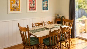 Comedor con mesa y sillas de madera, carteles enmarcados en la pared y vistas al exterior por una ventana.