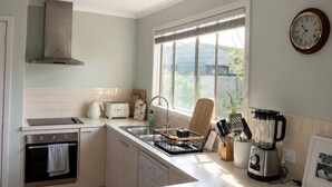 Una cocina moderna con horno empotrado, un lavamanos, una ventana con persianas y un reloj en la pared.