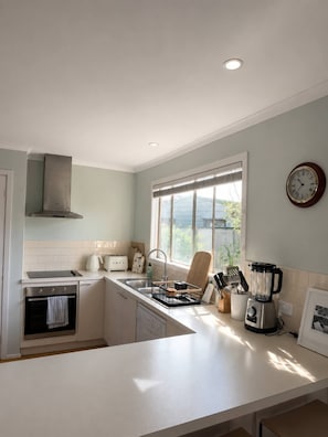 Een moderne keuken met een inbouwoven, een spoelbak, een raam met zonwering en een klok aan de muur.