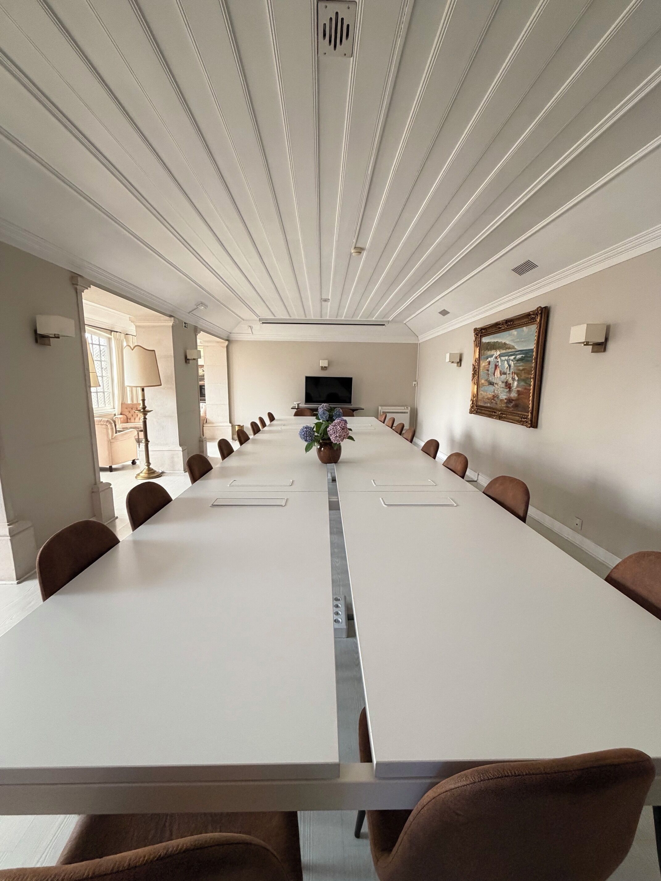 A conference room with a long table, chairs, a TV, and a painting on the wall.