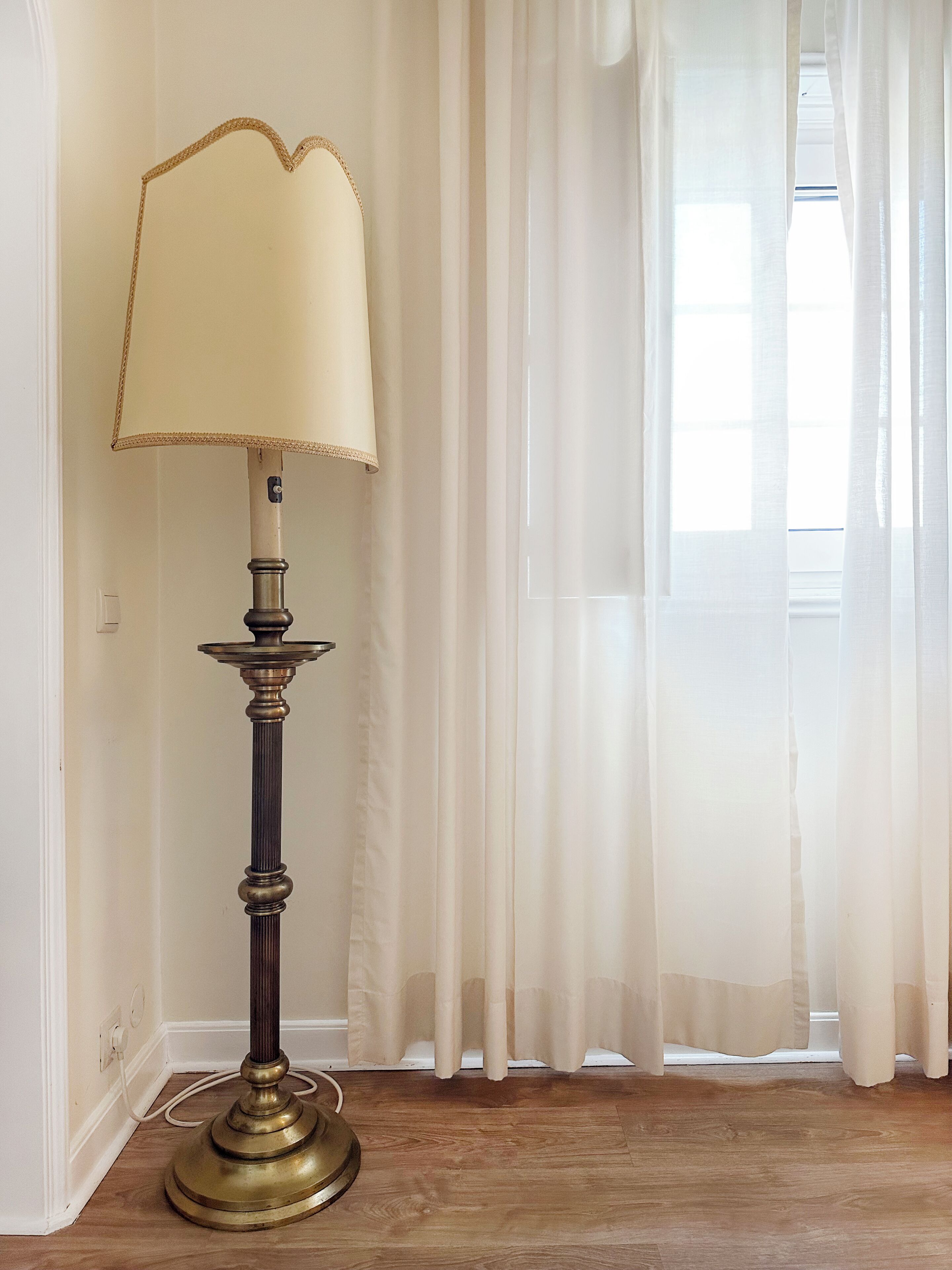 Um abajur com cúpula em um quarto com janela e cortinas finas.