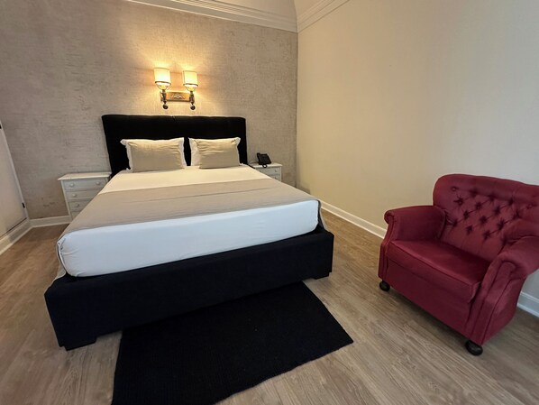 Un dormitorio con cama, mesitas de noche, un sillón rojo e iluminación instalada en la pared.