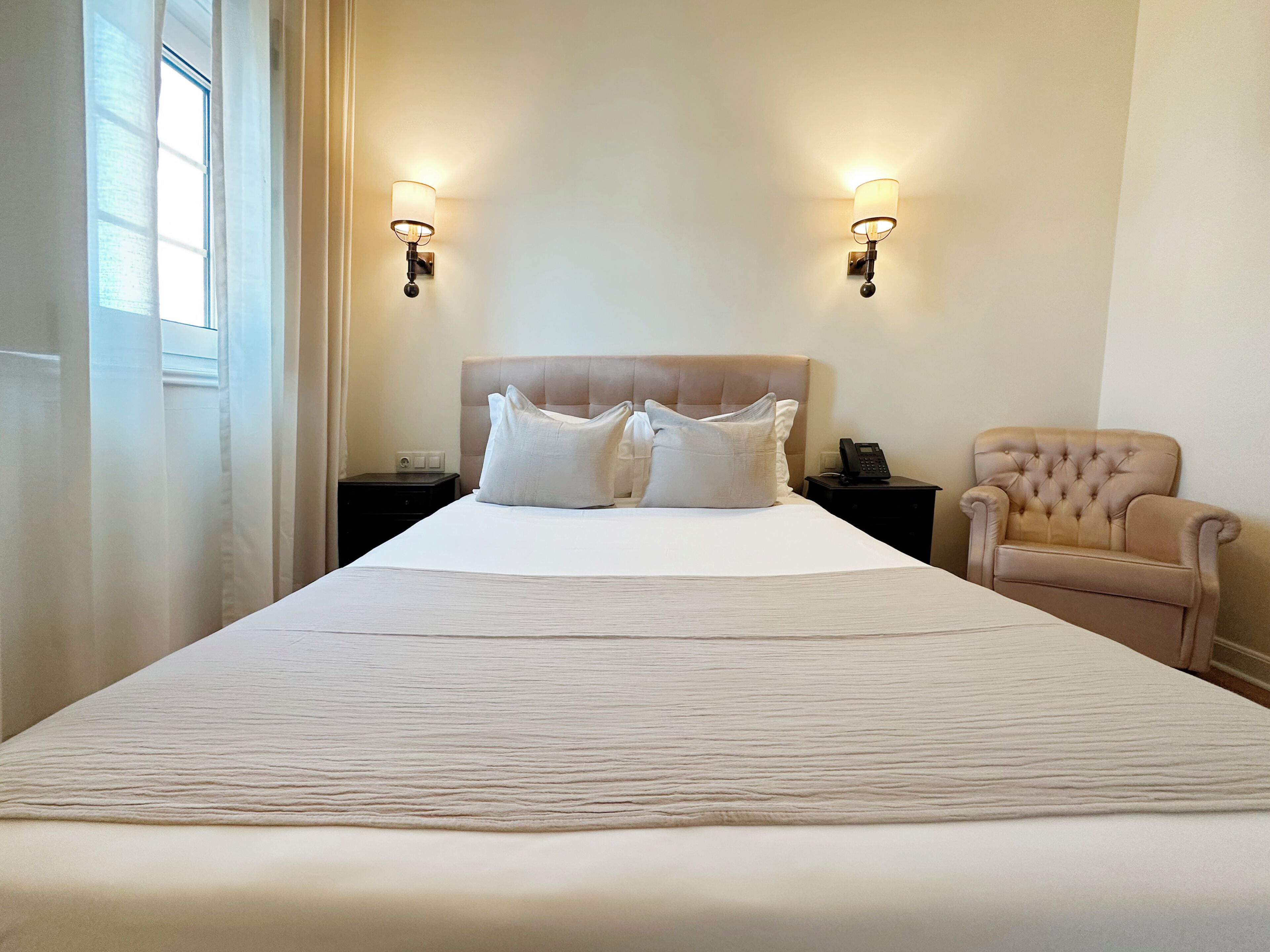 Habitaci ón de hotel con una cama grande, dos lámparas de noche, una silla y una mesita de noche con un teléfono.