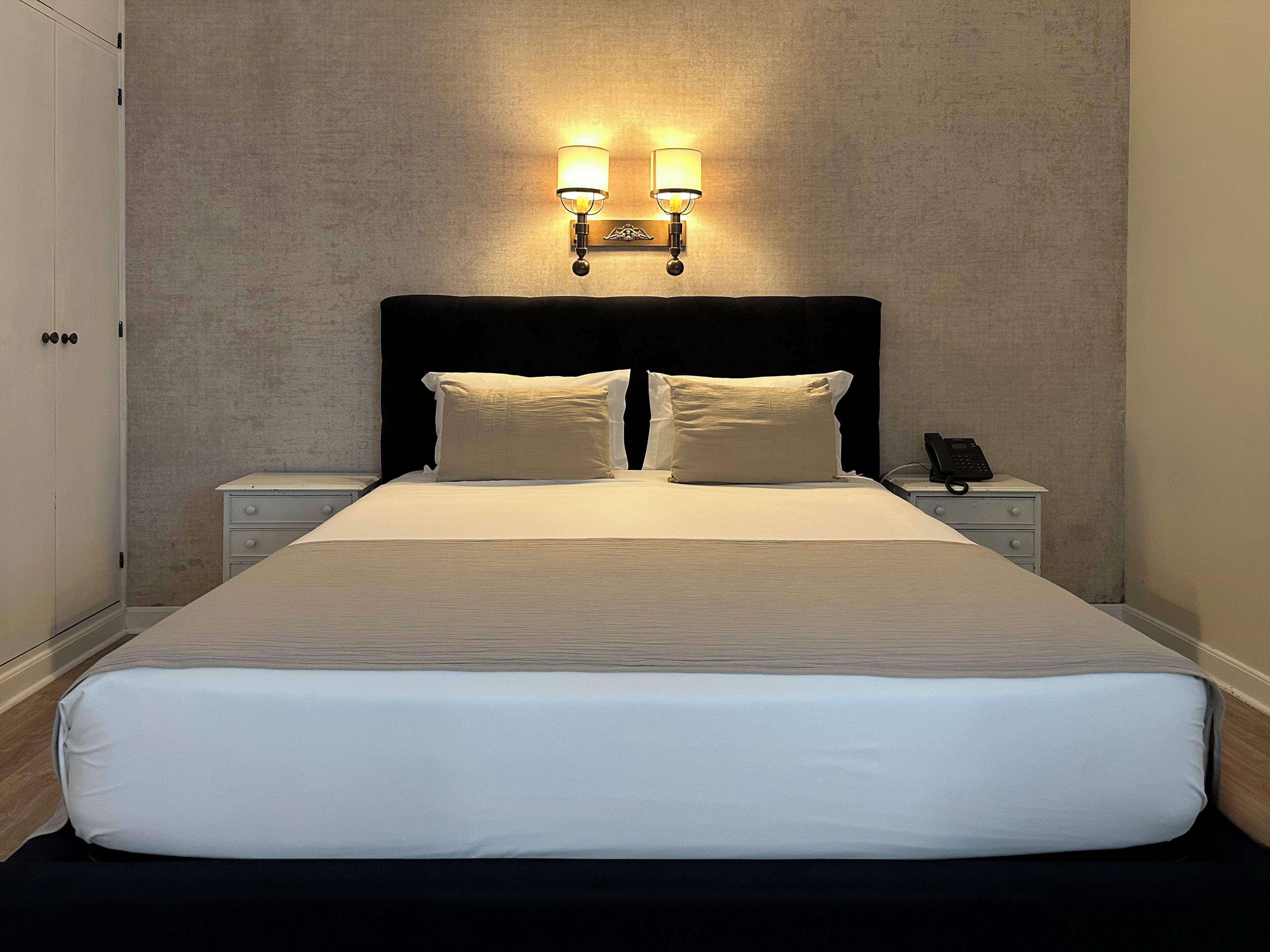 A neatly made bed with a headboard, two bedside tables, and a wall-mounted light fixture.