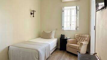 Una habitación con cama, una silla, una mesita, televisor en la pared y una ventana.