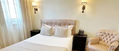 A hotel room with a large bed, two bedside tables, a chair, and a lamp.