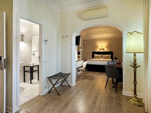 Quarto de hotel com cama, secretária, cadeira e uma pequena mesa.