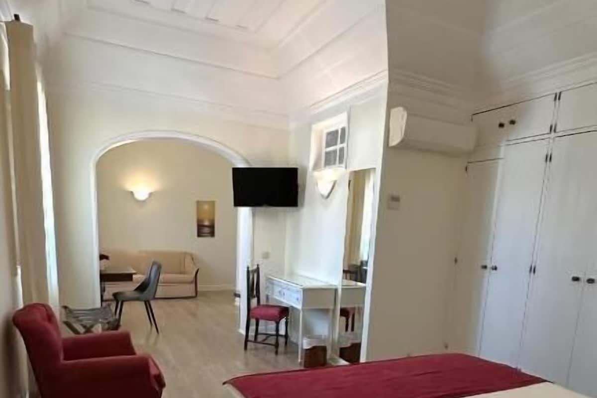 A room with a bed, a red chair, a desk, and a television.