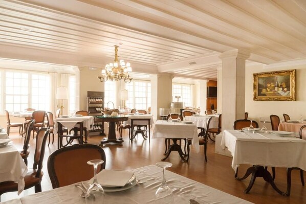 A dining area with tables set for service, a chandelier, and a framed painting on the wall. - Hotel João Padeiro (Aveiro)