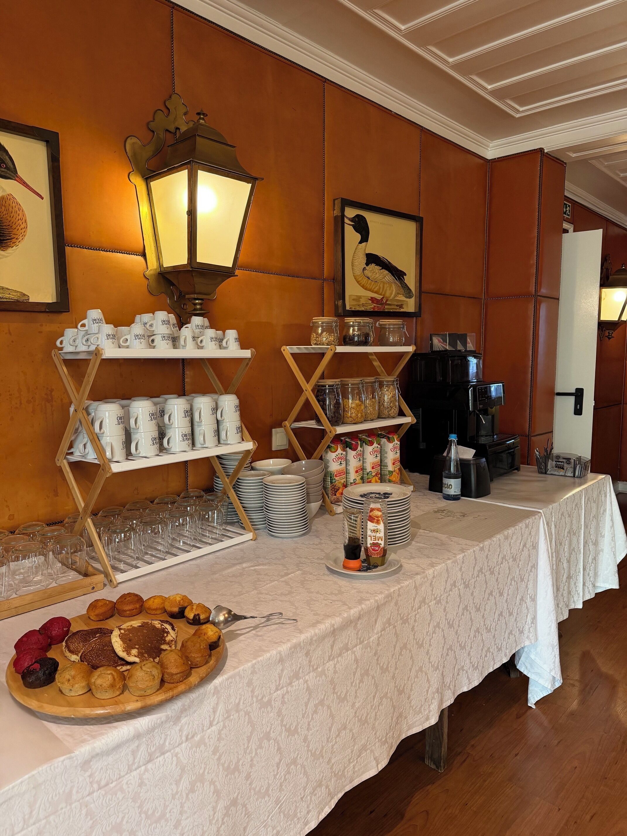 Montaje de bufé con diversos alimentos, máquinas de café y una pared decorativa con obras de arte enmarcadas.