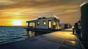 A waterfront building with a flat roof, large windows, and a staircase leading to an upper deck. - Floating house with fireplace on the lagoon (Ribnitz-Damgarten)