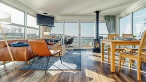 A modern living room with a sofa, chairs, a dining table, and a TV. - Floating house with fireplace on the lagoon (Ribnitz-Damgarten)
