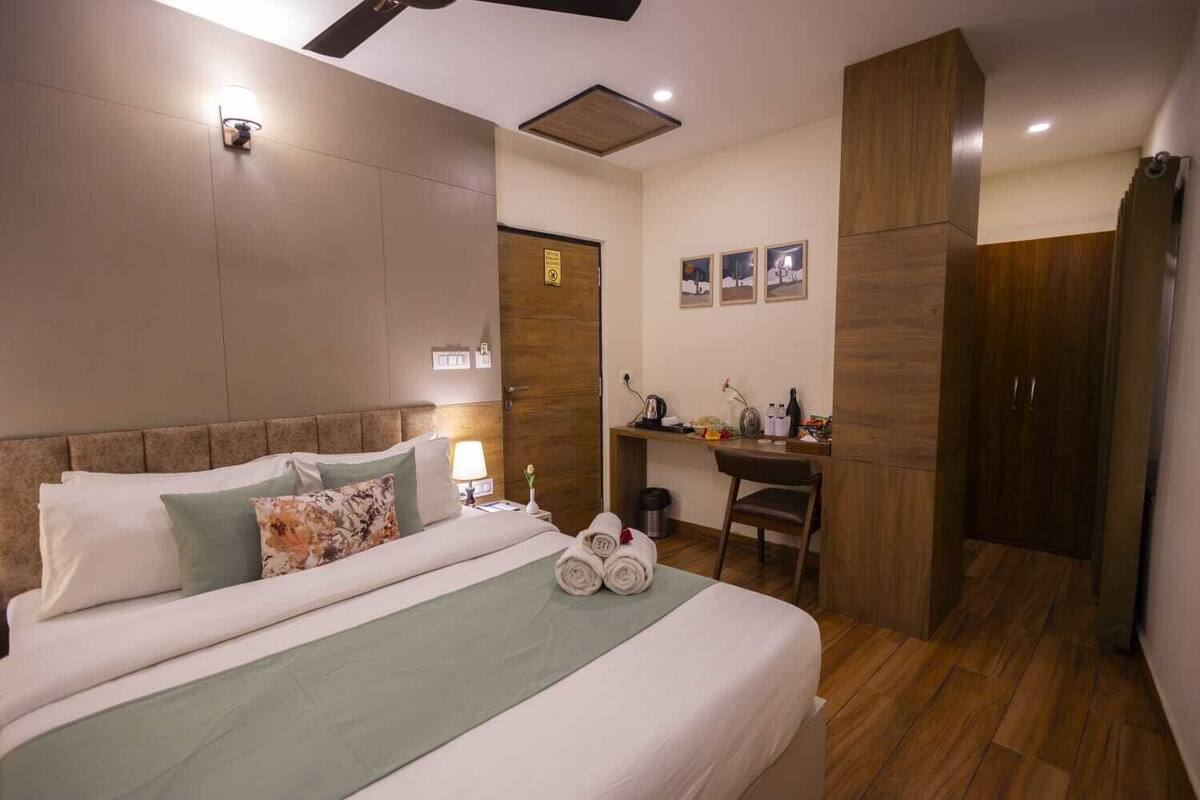 Una habitación de hotel con cama, escritorio, silla, armario y una lámpara fijada a la pared.