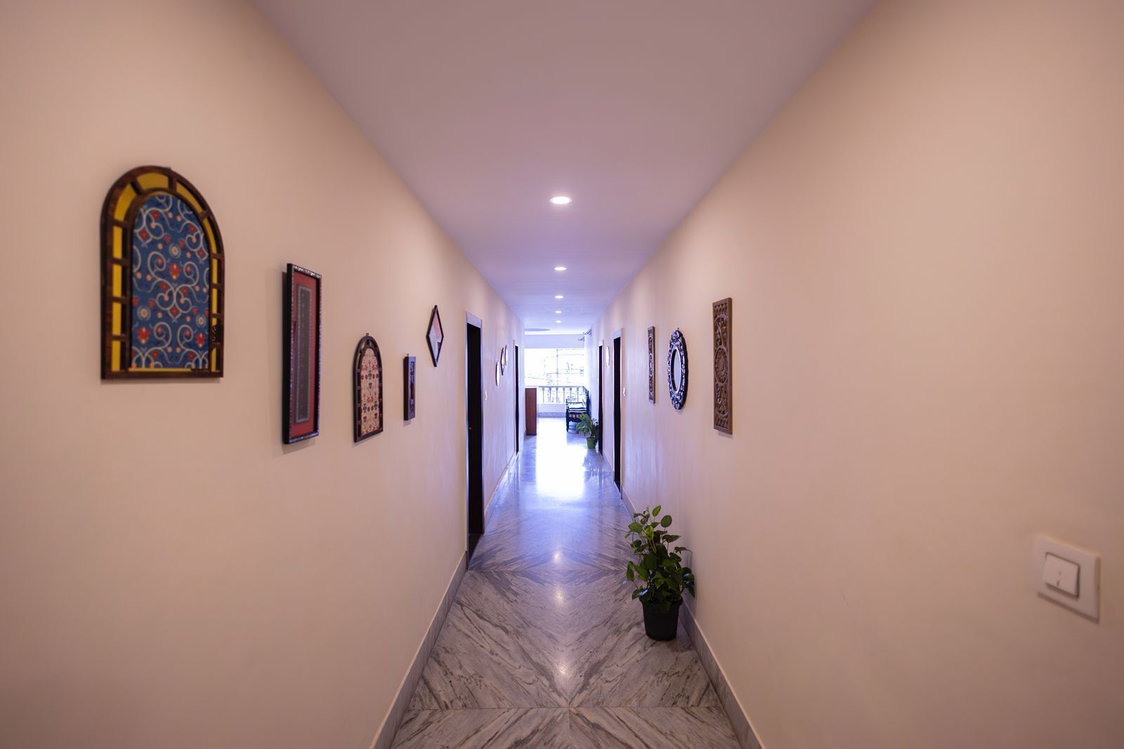 A hallway with a marble floor, framed artwork on the walls, and a potted plant.