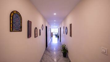 A hallway with a marble floor, framed artwork on the walls, and a potted plant.