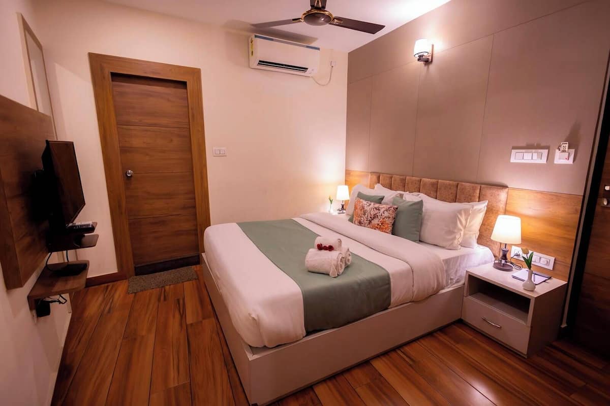 Habitación de hotel con cama, mesita de noche, lámpara, aire acondicionado y televisor.