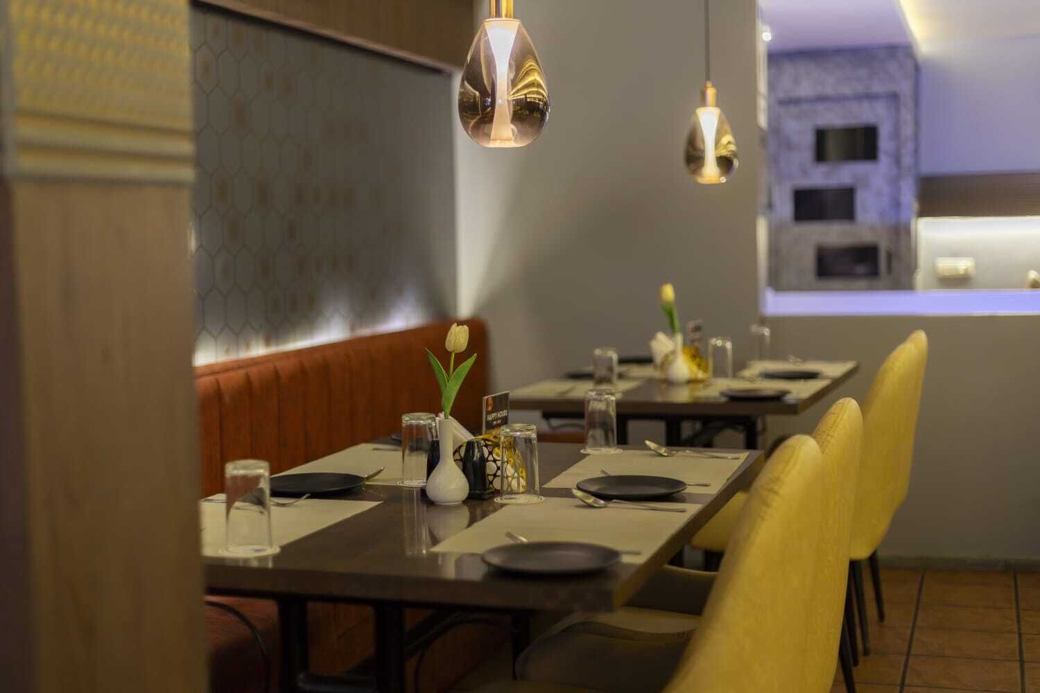 Un restaurante con mesas dispuestas para comer, un jarrón con una flor y lámparas colgantes.