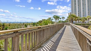 A wooden boardwalk leading to a beach with palm trees and a high-rise building in the background. - Kingston Plantation-Sleeps 6-2bed/2bath-Full Kitchen-Laundry-Lake View (Myrtle Beach)