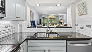 A modern kitchen with white cabinets, stainless steel appliances, a double sink, and a black countertop. - Kingston Plantation-Sleeps 6-2bed/2bath-Full Kitchen-Laundry-Lake View (Myrtle Beach)