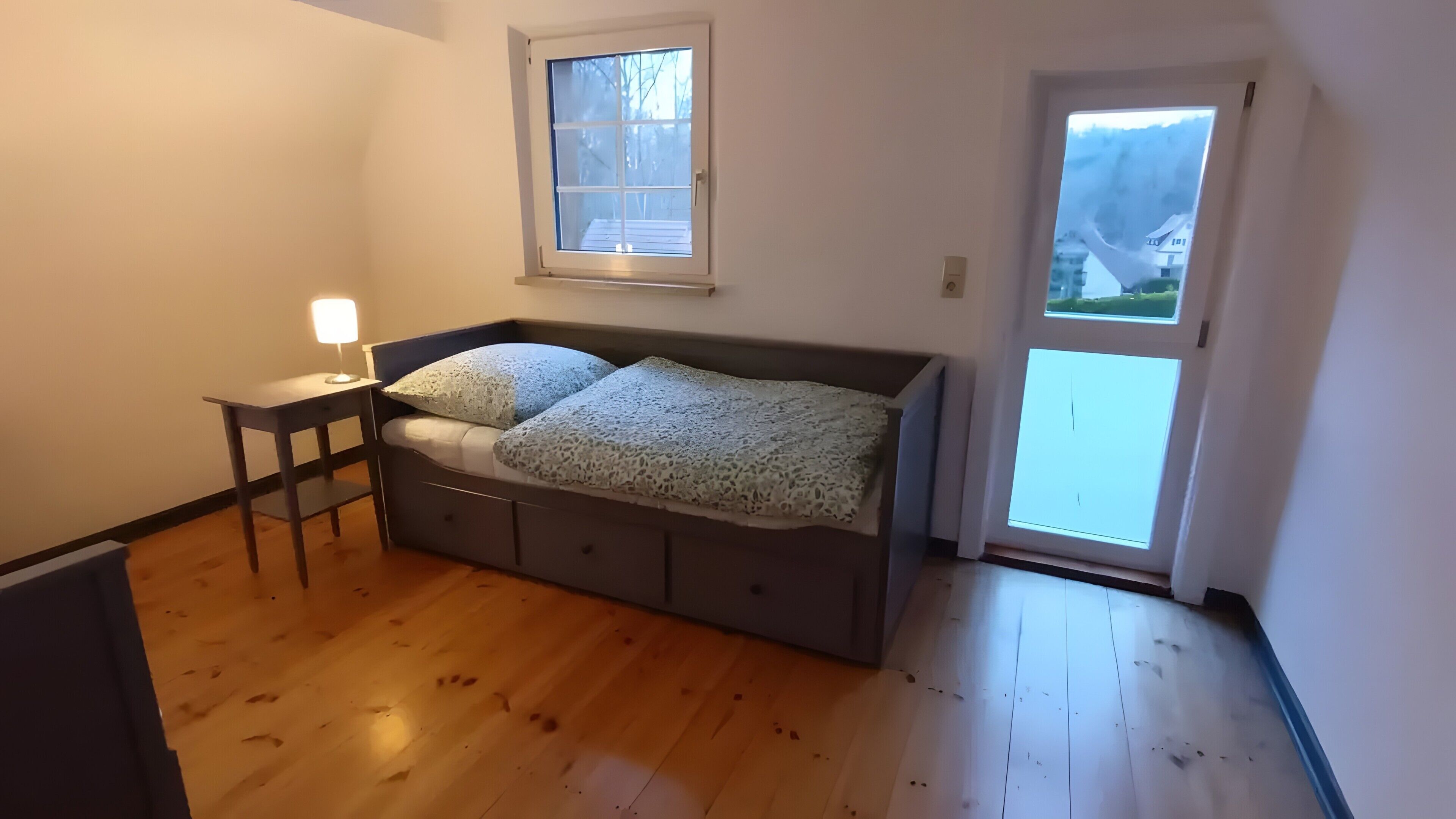 Une chambre à coucher avec un lit, une table de chevet, une fenêtre et une porte.