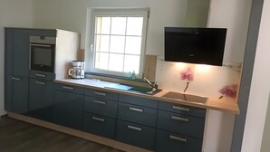 A modern kitchen with a built-in oven, a coffee maker, and a window with blinds.