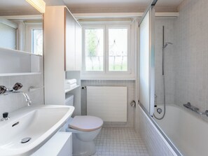 Un baño con lavamanos, inodoro y ducha blancos. Hay un ventanal sobre el inodoro.