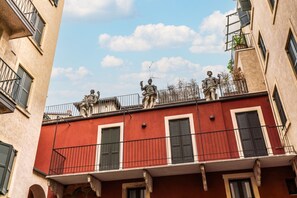 Ein Gebäude mit roter Fassade, Balkonen mit schwarzen Geländern und Statuen auf dem Dach.